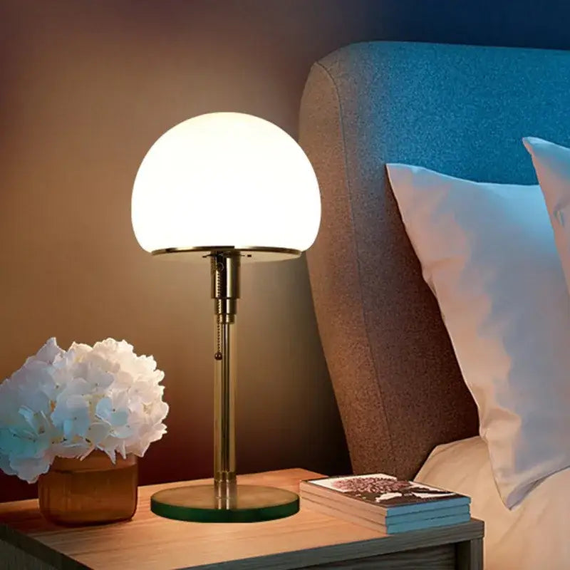 A bauhaus mushroom table lamp with a frosted milk white glass shade and brass-finished metal base for bedroom lighting