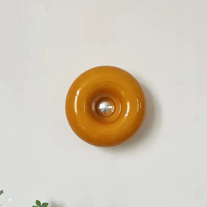 A glossy amber glass decorbites donut wall lamp with metallic center ideal as a Bauhaus style bedroom wall lamp