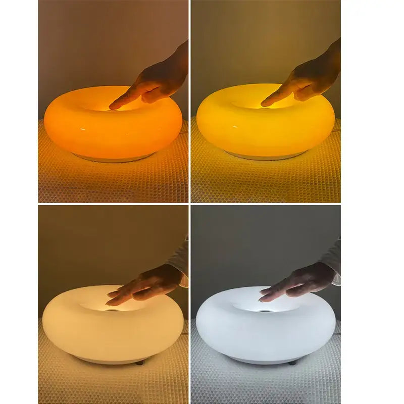 A sleek glass table lamp with a ring-shaped orange glass body emitting warm or cool light for bedroom use