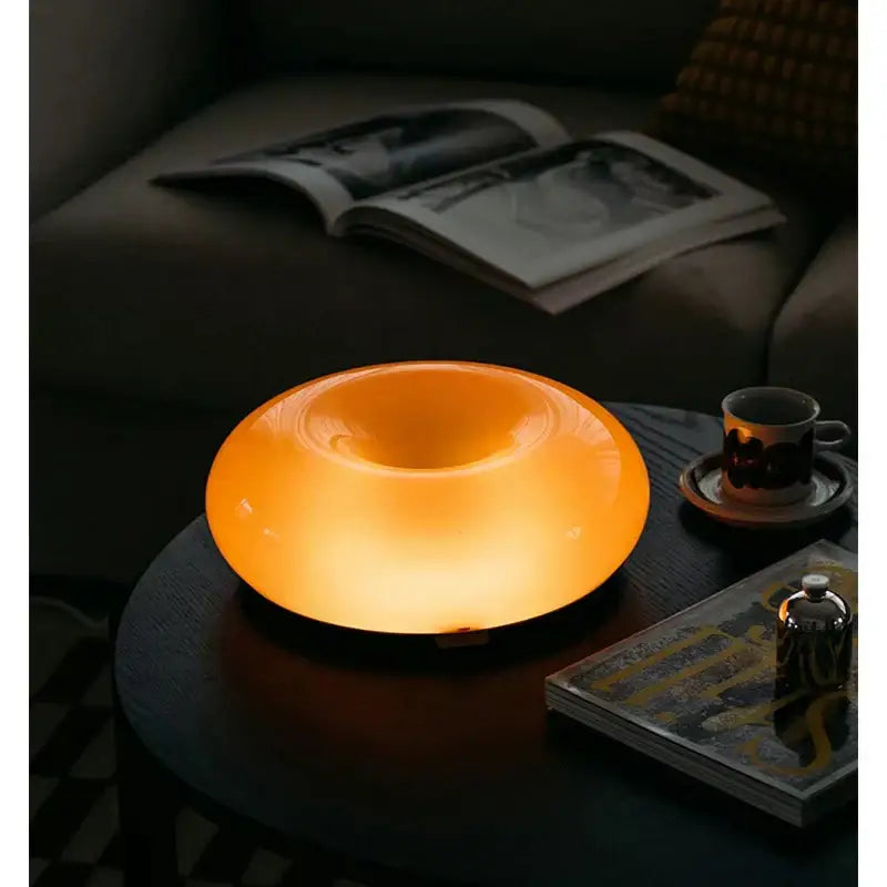 A bauhaus orange glass style orange glass table lamp with a glowing translucent bowl shape for bedroom accessory
