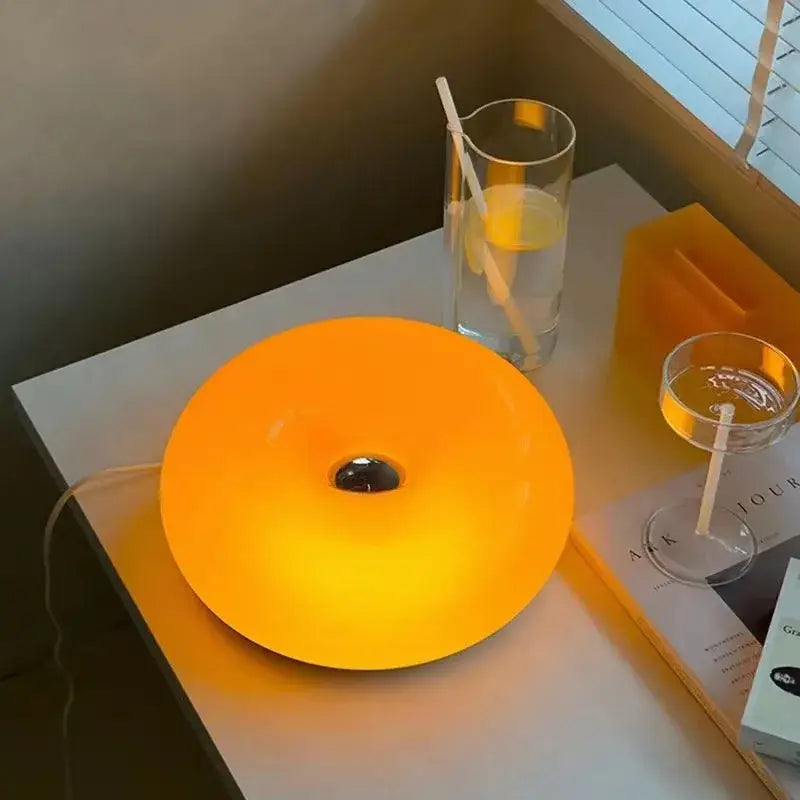 Bauhaus orange glass table lamp with a glowing glossy finish and central dark hole ideal for bedroom use