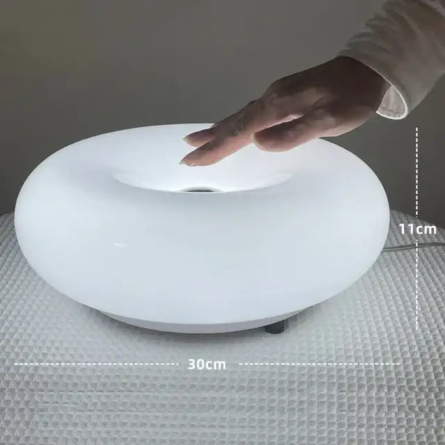 A sleek white oval led table lamp with a glossy finish and circular indentation for use with bauhaus orange glass table lamps