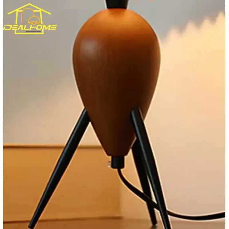 A bauhaus pleated wood table lamp with a sleek teardrop shape warm brown finish and black metal tripod legs