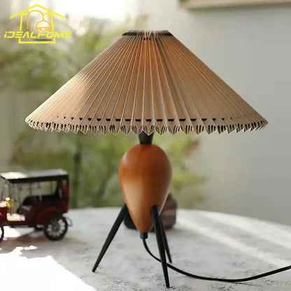 A warm-toned bauhaus pleated wood table lamp with accordion-style shade and tripod base for bedroom or desk use