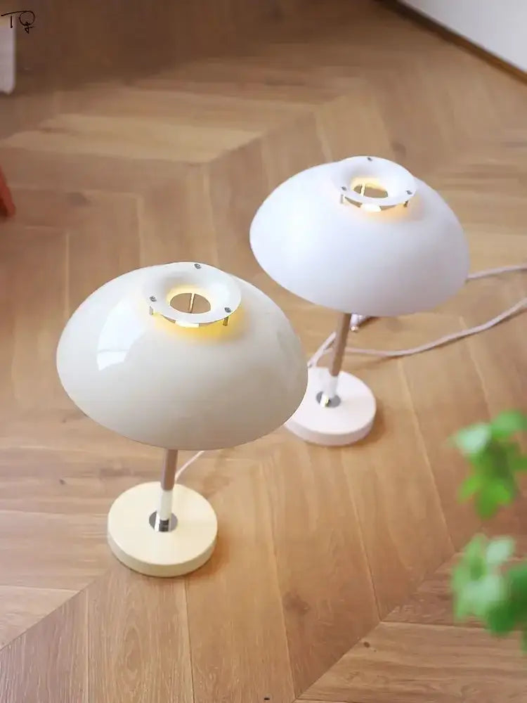 Two minimalist white bauhaus led table lamps with glossy ceramic bases and metallic stems emitting warm light