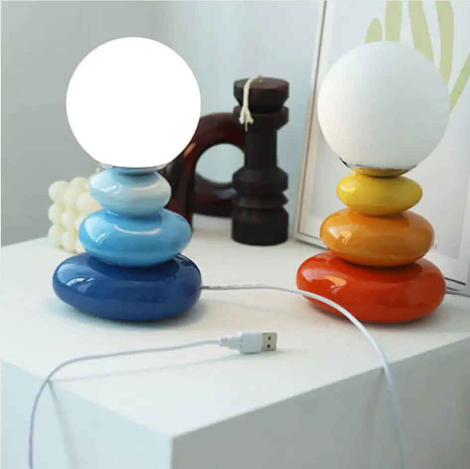 Two stacked glossy ceramic bauhaus table lamps with spherical shades in vibrant color gradients for modern design