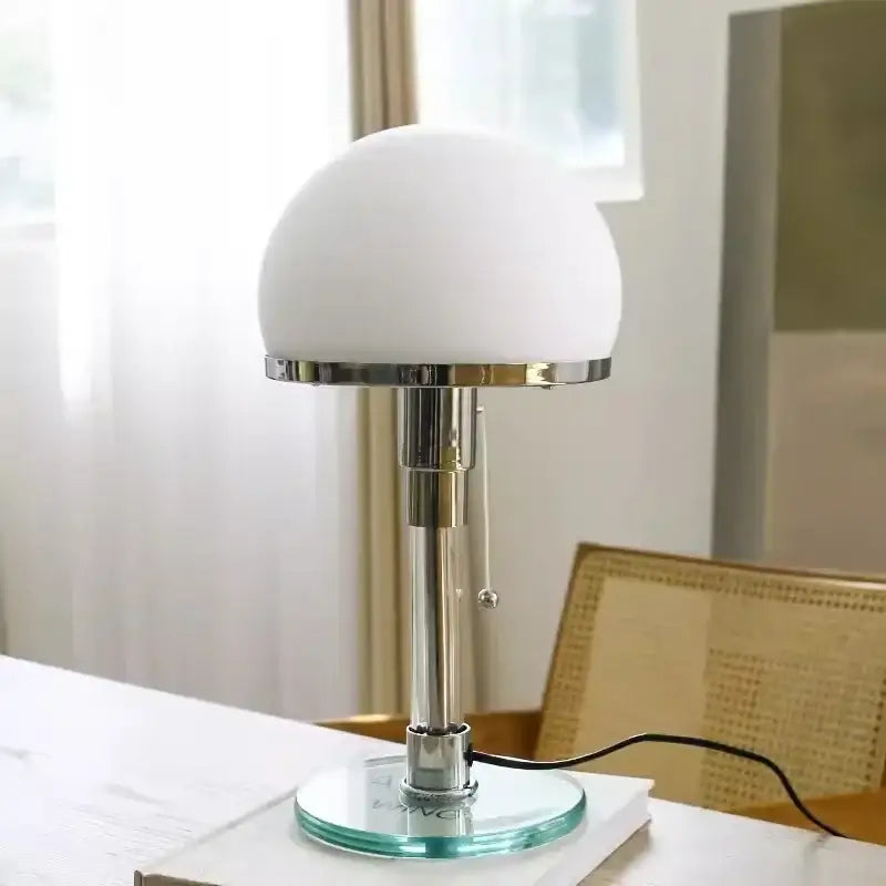 A sleek bauhaus glass ball desk lamp with a frosted white dome shade and polished chrome base for bedroom use