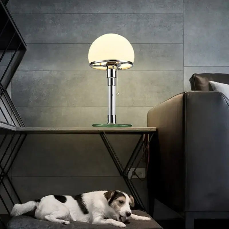 A sleek bauhaus glass ball desk lamp with frosted white glass shade and polished chrome stem for bedroom use