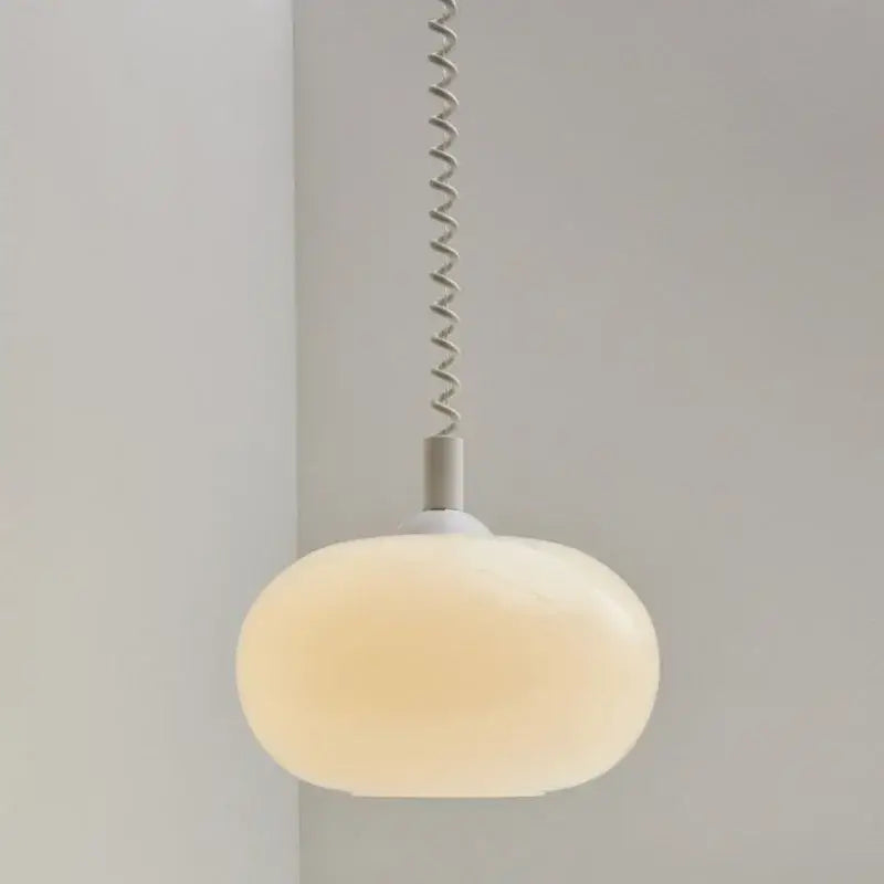 A bauhaus glass pendant light with a soft frosted white oval shade and metallic spiral chain for dining room