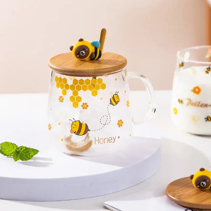 Clear glass bee glass spoon milk cup with yellow bee illustrations and bamboo lid topped by bear bee figurine