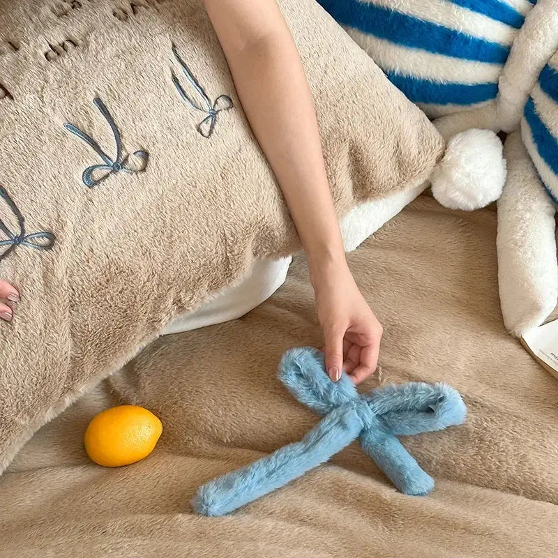 A soft light blue fuzzy bow accessory with plush texture complementing beige and blue embroidered velvet duvet bedding set