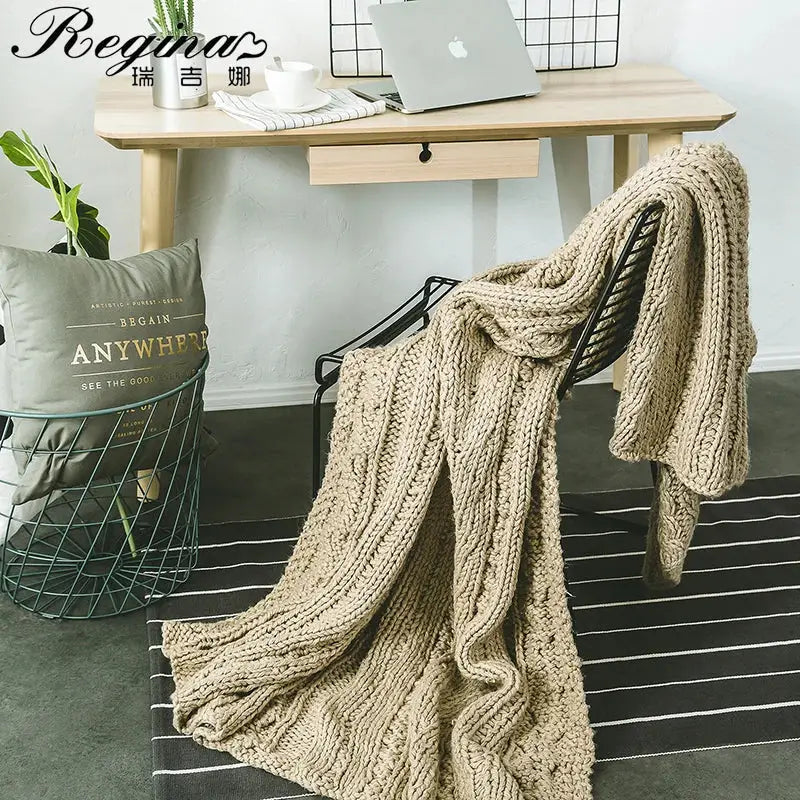 A decorbites beige chunky knit throw blanket with tassels draped over a black metal chair for cozy bedroom decor
