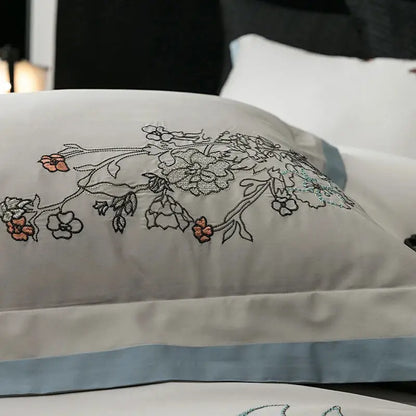 A delicate white pillow sham with peach and silver floral embroidery and light blue satin border in decorbites cotton flowers bedding set