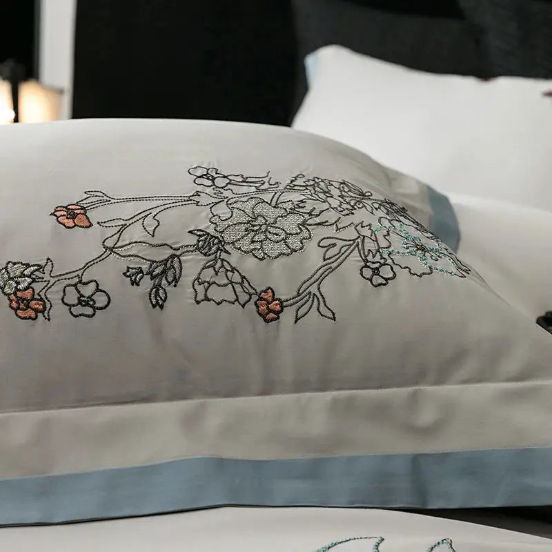 A delicate white pillow sham with peach and silver floral embroidery and light blue satin border in decorbites cotton flowers bedding set