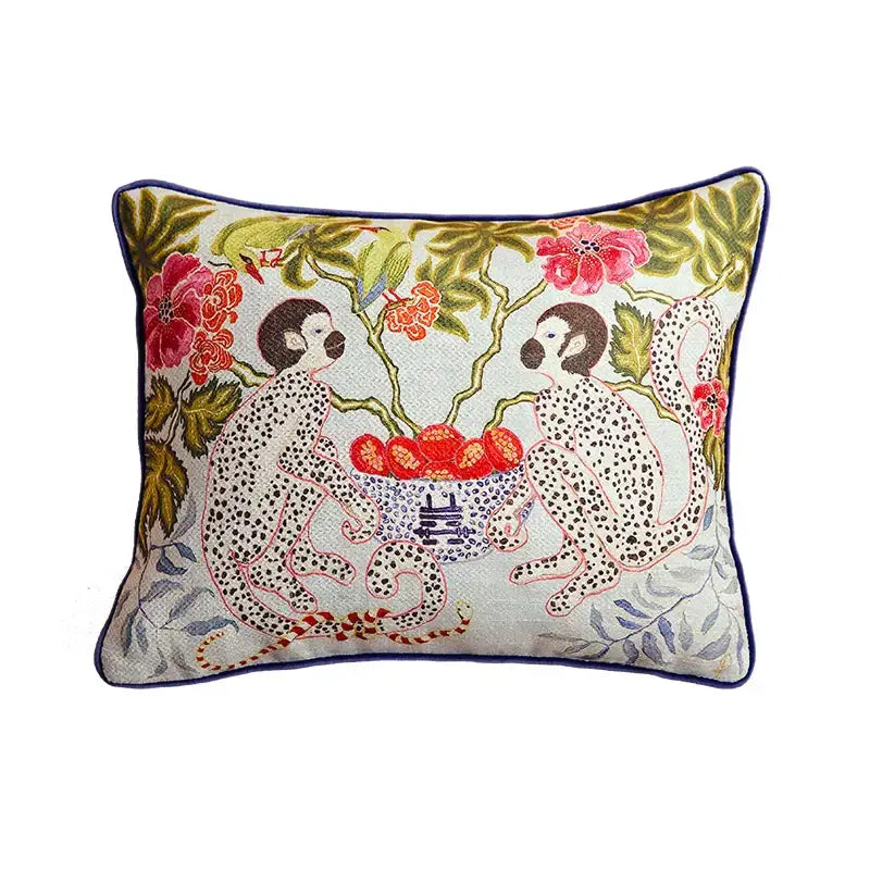 Beige pillow case with embroidered spotted monkeys and floral design framed by navy blue piping for living room sofa