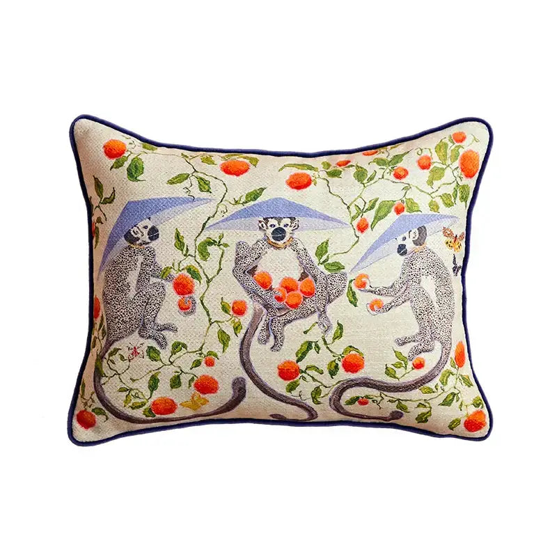 Beige pillow case with embroidered lemur design, orange fruit, green vines, and navy blue piping for living room sofa