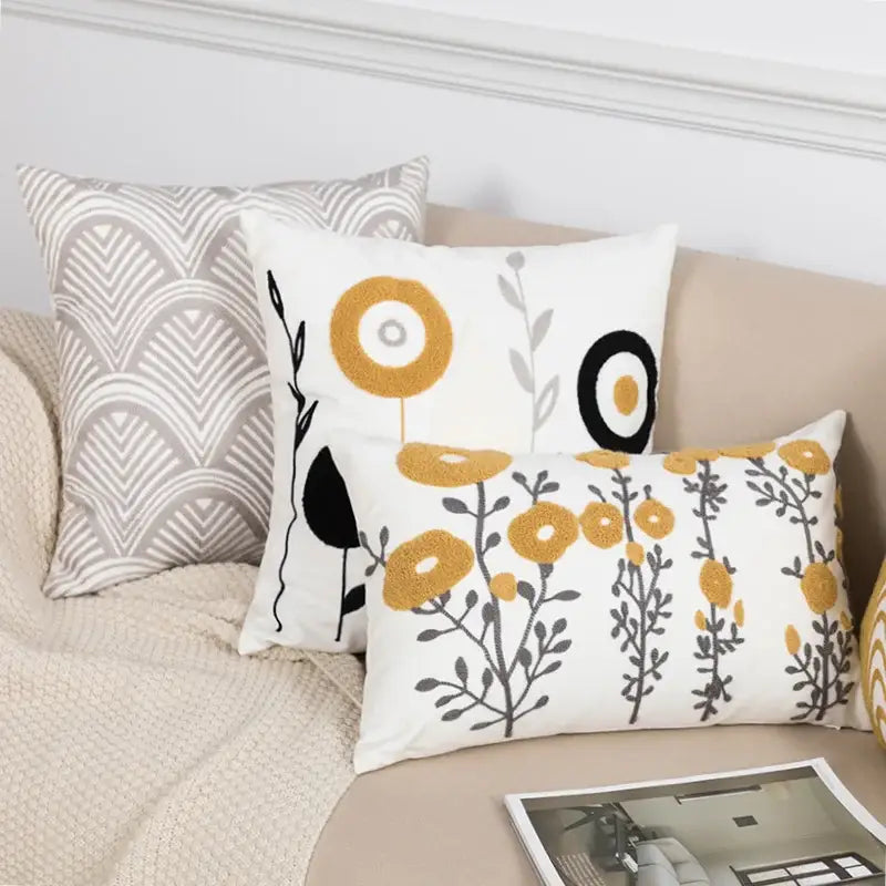 Beige pillow cover with embroidered daisy floral design featuring yellow and black flowers and gray stems for bedroom decor