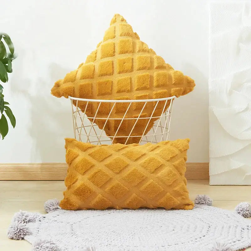 A mustard-yellow textured cushion cover with geometric diamond pattern made of soft plush material in a wire basket
