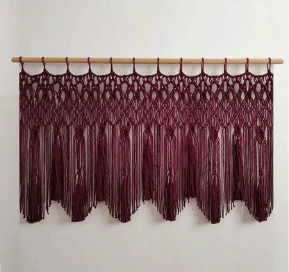 A maroon decorbites handwoven macrame wall hanging with intricate knotwork and tassels suspended from a light wood rod