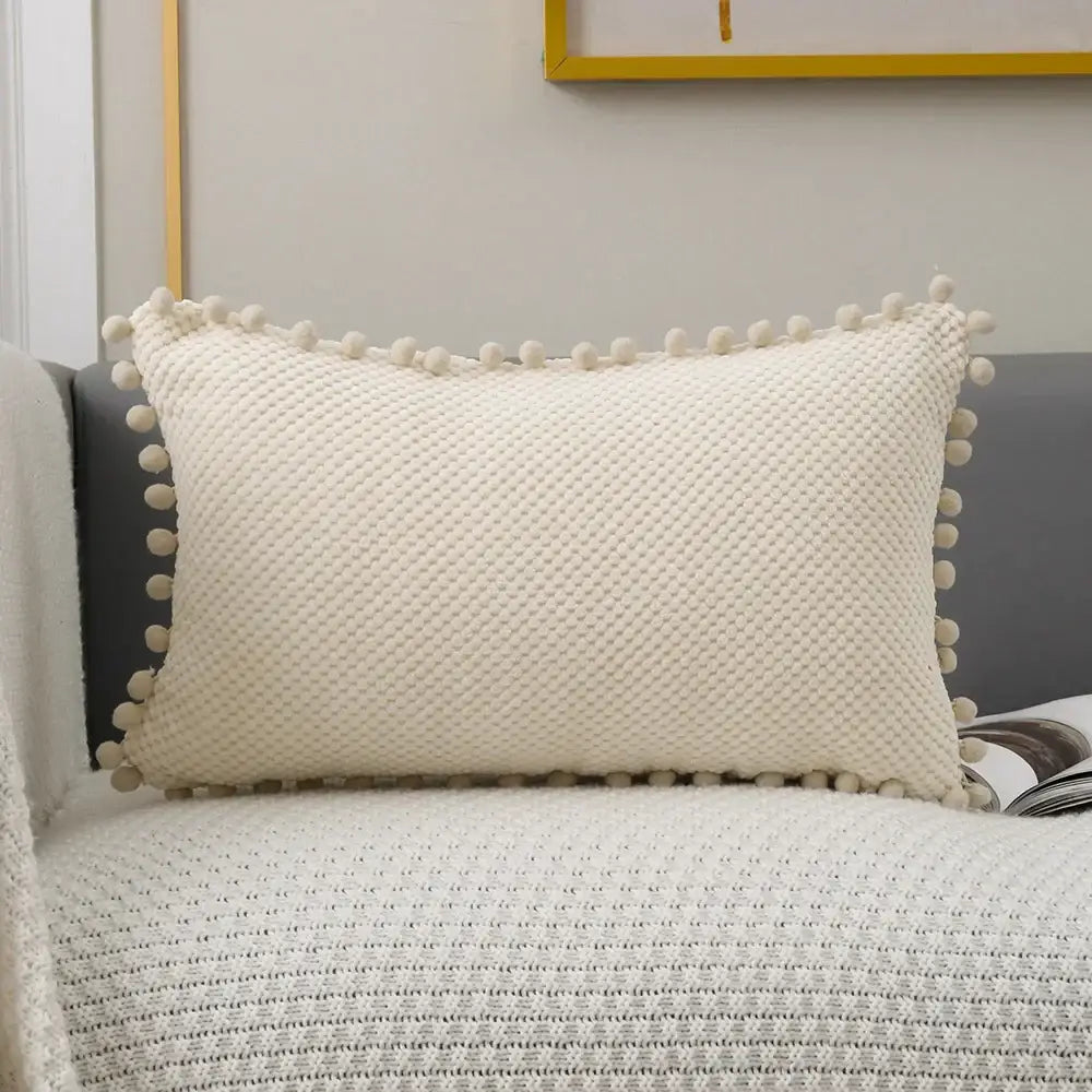 Cream-colored knit decorative pillow cover with textured diamond pattern and pom-pom trim for living room decor