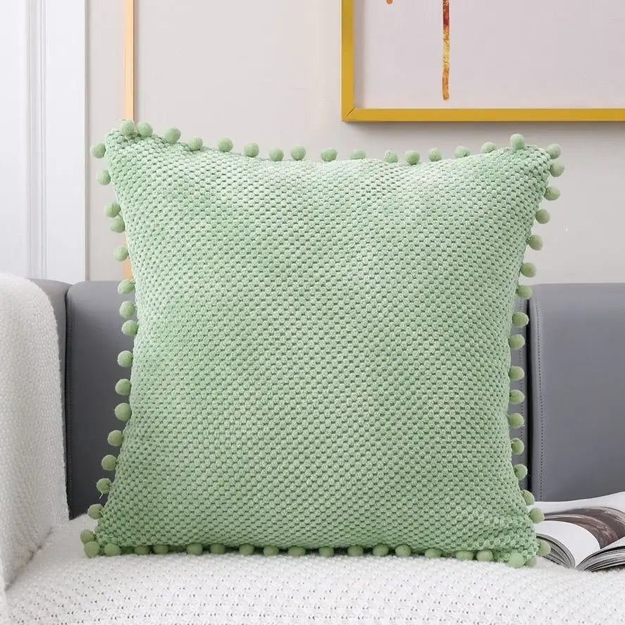 Light green knitted decorative pillow cover with textured woven pattern and pom-poms for living room decor