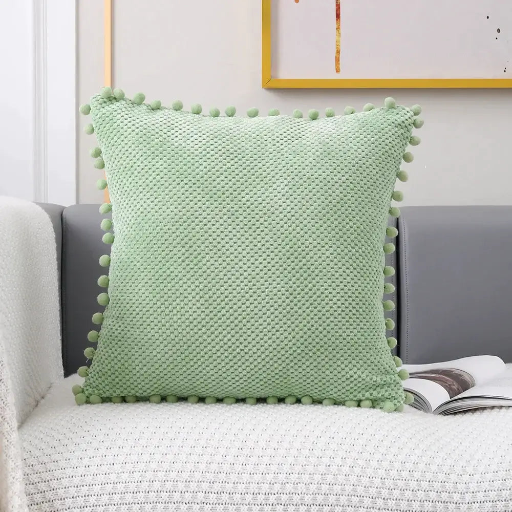 A soft mint green knitted decorative pillow cover with textured pattern and pom-poms for living room decor
