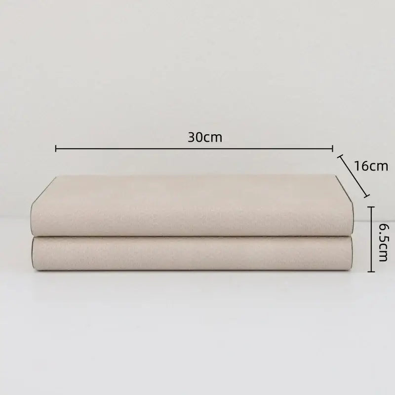 A neatly folded beige linen duvet cover set measuring 30cm by 16cm with 6.5cm thickness beside decorbites beige leather jewelry box storage container with silver hinges
