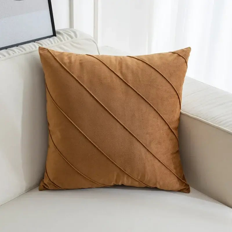 A square tan suede pillow with diagonal stitched seams featuring hand pleat embroidered details for living room decor