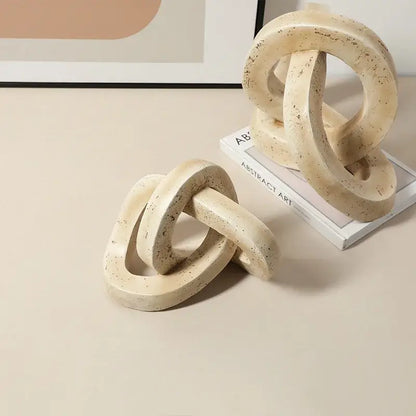 Beige speckled geometric interlocking loop knot sculpture in cream-colored textured concrete for living room decor