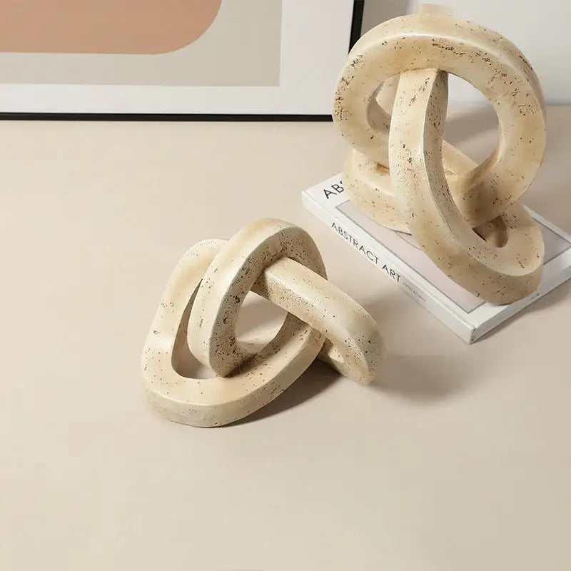 Beige speckled geometric interlocking loop knot sculpture in cream-colored textured concrete for living room decor