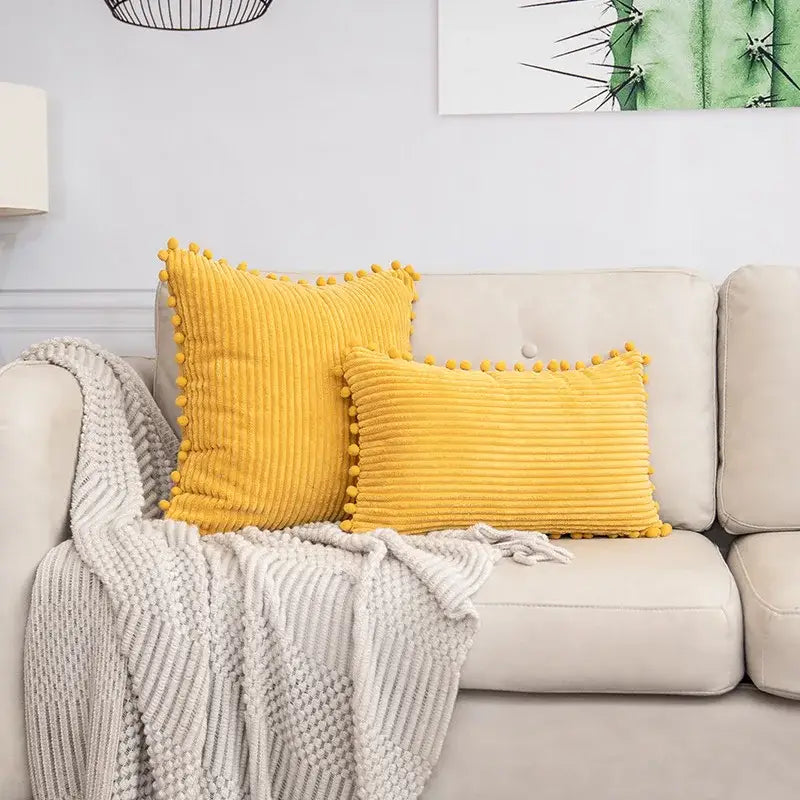 Two mustard-yellow corduroy throw pillows with pom pom trim matching decorbites beige striped cushion cover