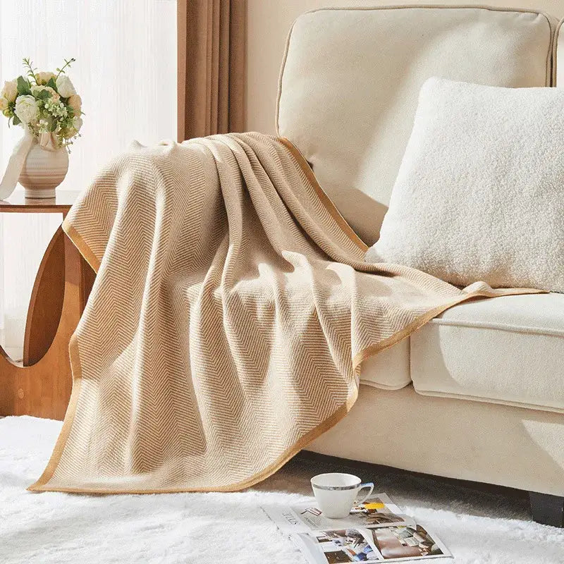 Beige and tan decorbites herringbone knit blanket with subtle tan border draped on cream sofa for living room decor