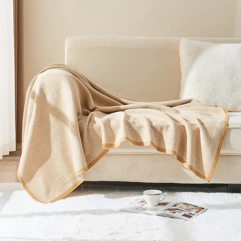 Beige and tan decorbites herringbone knit blanket with gold border draped over sofa for living room decor