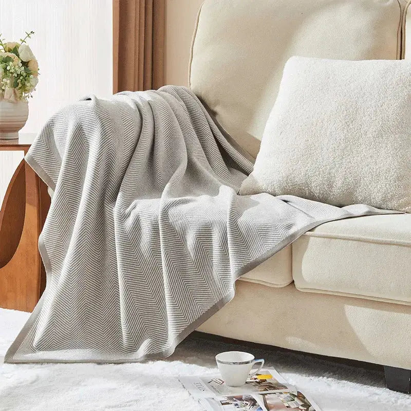 Beige and tan herringbone knit blanket by decorbites draped over a sofa arm in a living room setting