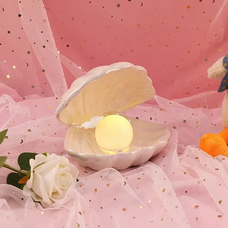 A soft pink decorbites ceramic shell pearl night light with a glowing yellow orb for bedroom decor