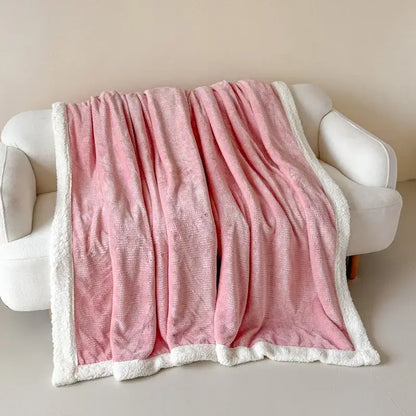 A soft pink fleece blanket with plush white sherpa border draped on a white sofa decorbites cozy lamb wool blanket