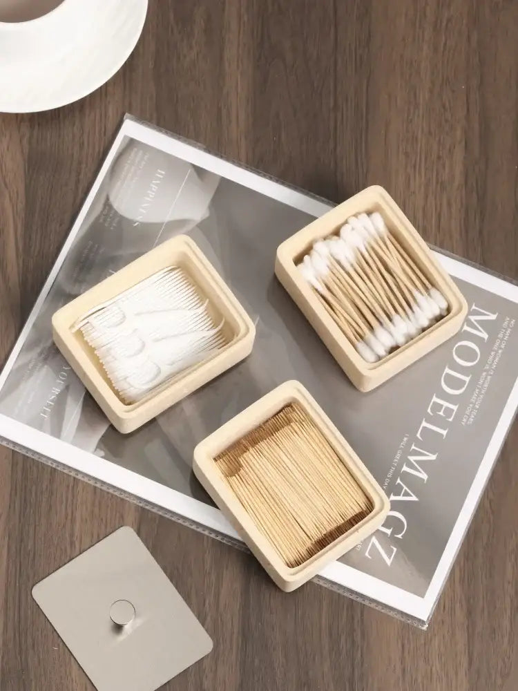 Three square light beige wooden containers holding cotton swabs and toothpicks complement a beige textured natural stone double decker jewelry organizer