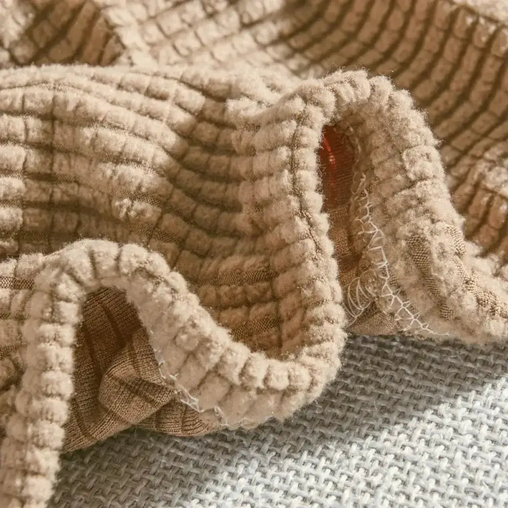 Beige textured quilted sofa cover with pillows made of beige corduroy fabric featuring ribbed texture and elasticized hem