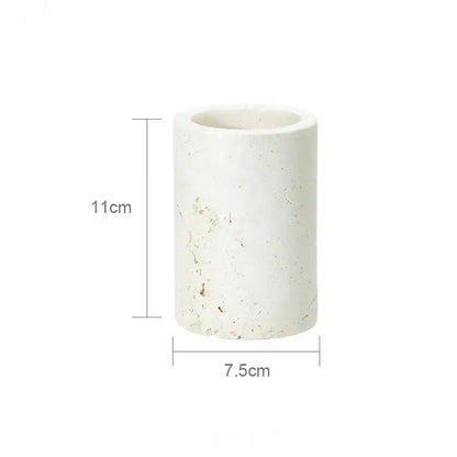 A cylindrical white concrete planter with a textured speckled surface in a beige travertine marble bathroom set