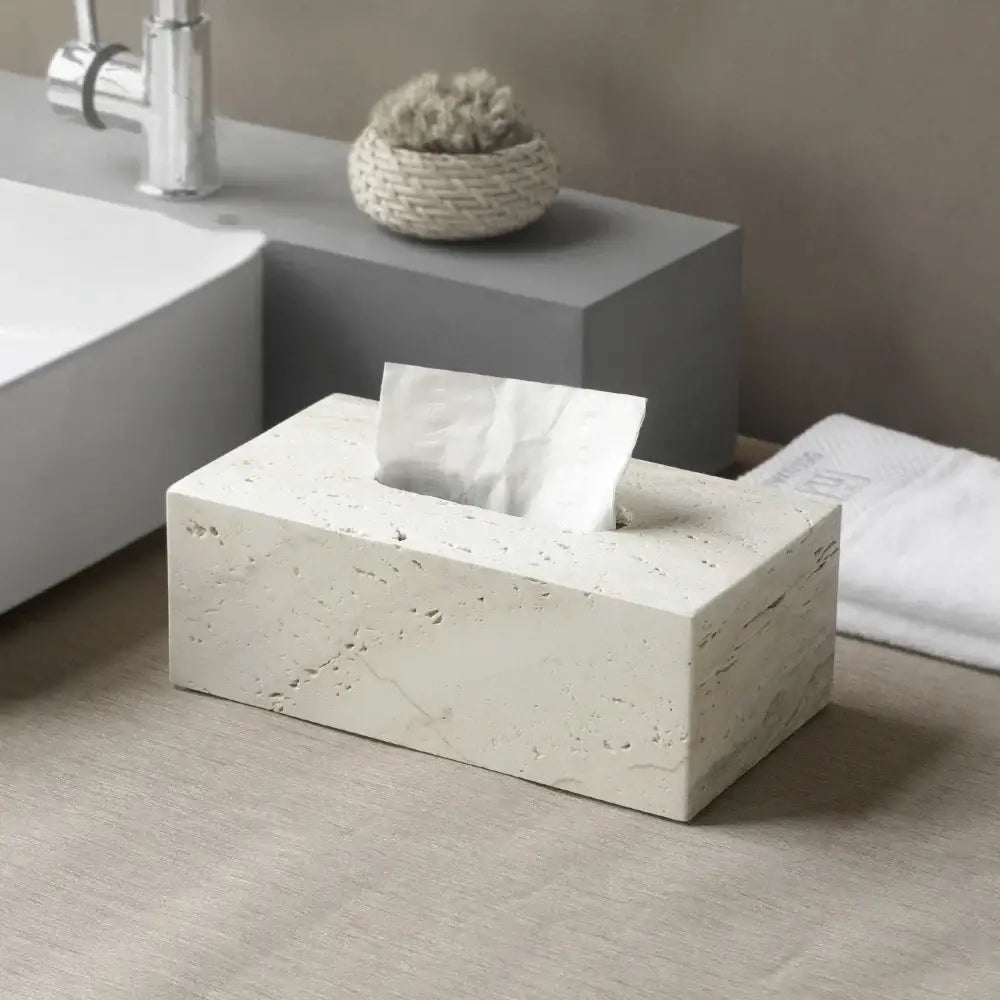 A beige travertine marble rectangular tissue box with textured stone surface and white tissue partially pulled out