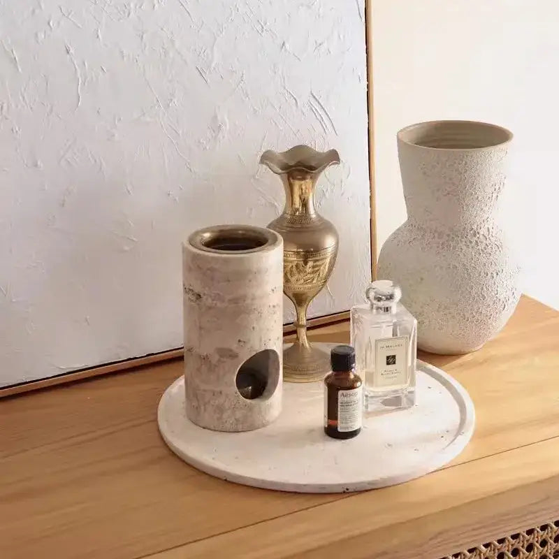 Beige travertine stone essential oil burner with circular cutout on side resting on matching round tray oil burner diffuser