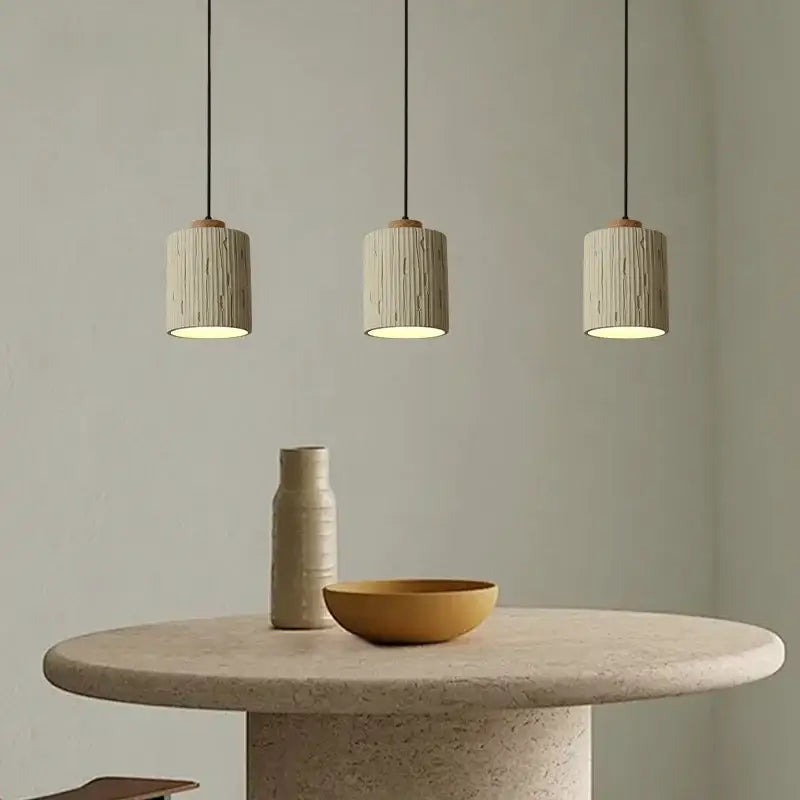 Three beige columnar micro cement pendant lights with wood accents hang above a stone table for kitchen decorbites decor