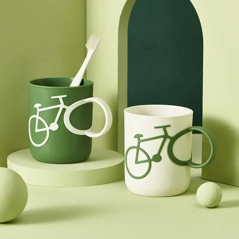 Green and white ceramic toothbrush holder cup featuring bicycle designs molded into the handles for bathroom use