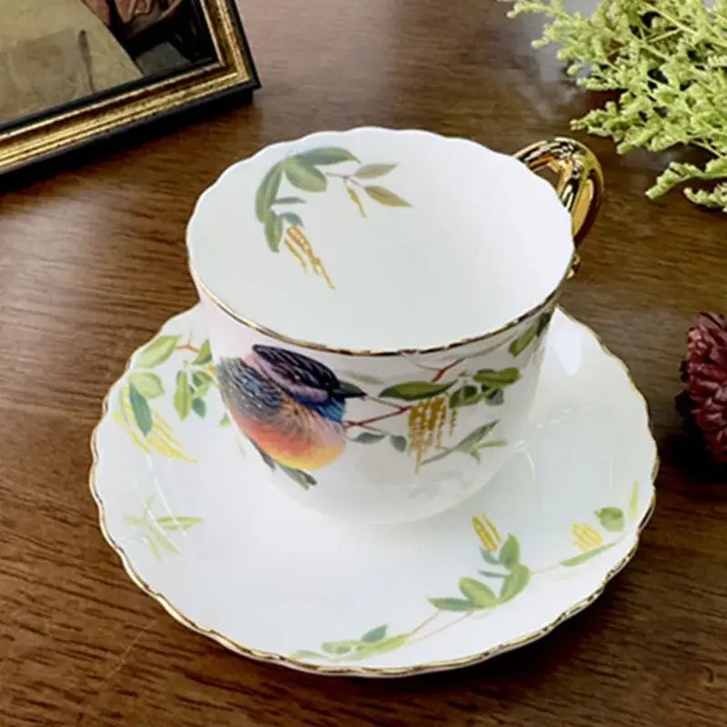 A delicate white porcelain bird pattern ceramic gold trimmed mug and saucer set featuring a decorbites bird design