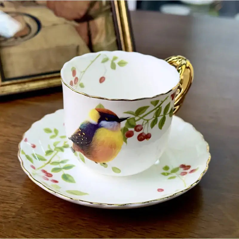 A delicate white porcelain bird pattern ceramic gold trimmed mug and saucer set featuring a colorful bird design