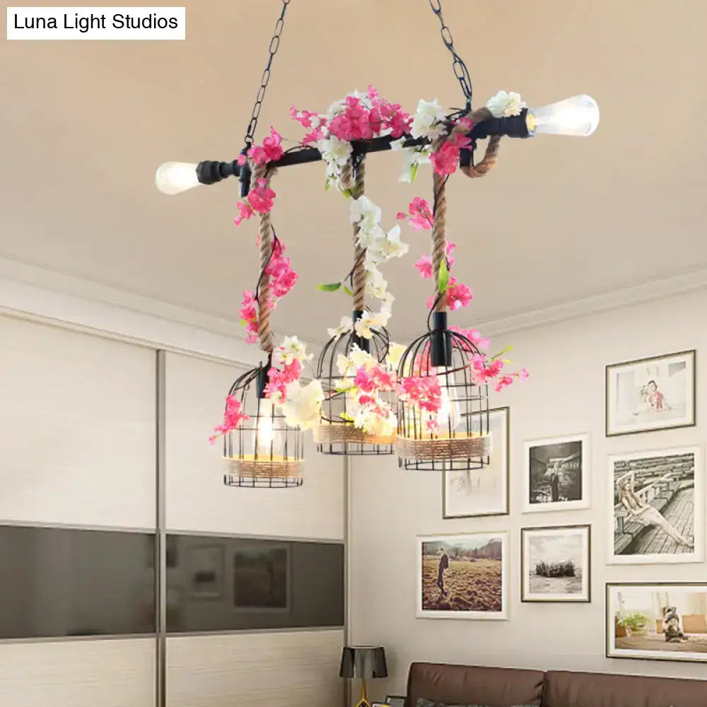 A rustic industrial chandelier with three black metal birdcage shades adorned with pink and white flowers in rose red