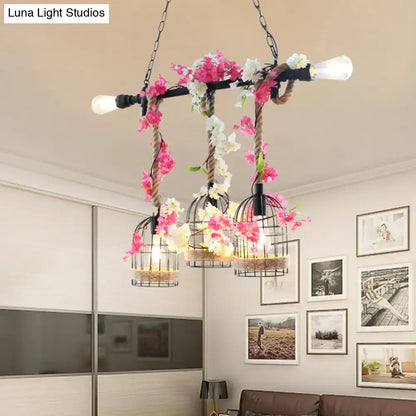 A rustic industrial chandelier with three black metal birdcage shades adorned with pink and white flowers in rose red