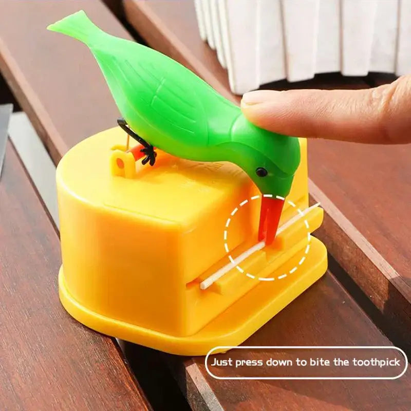 A bright green decorbites birdie toothpick holder with black eyes and red beak on a yellow plastic toothpick dispenser