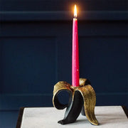 A vibrant pink candle in a decorative black and gold metallic banana candlestick holder for dining room decorbites golden banana decor
