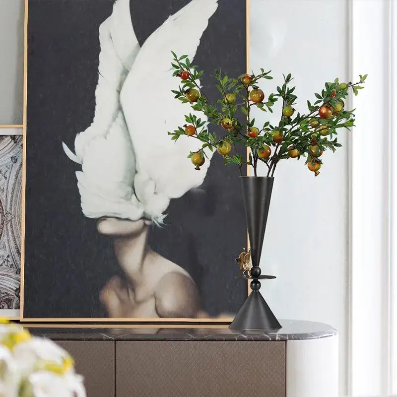 Black and gold decorbites bronze flower vase with conical shape and ornamental bird detail holding artificial branch